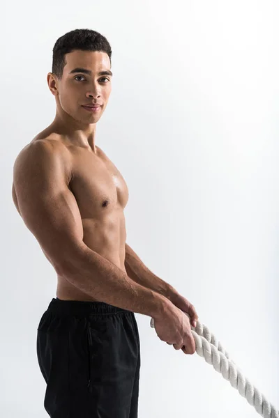 Handsome mixed race man with muscular torso holding ropes and looking at camera on white — Stock Photo