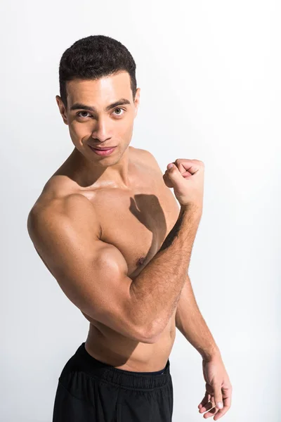 Bonito misto raça homem demonstrando bíceps e olhando para câmera no branco — Stock Photo