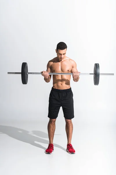 Athletic mixed race man in black shorts and red sneakers holding barbell on white — Stock Photo