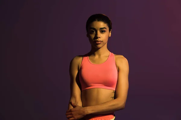 Beautiful sportive african american girl in pink sports bra looking at camera isolated on purple — Stock Photo