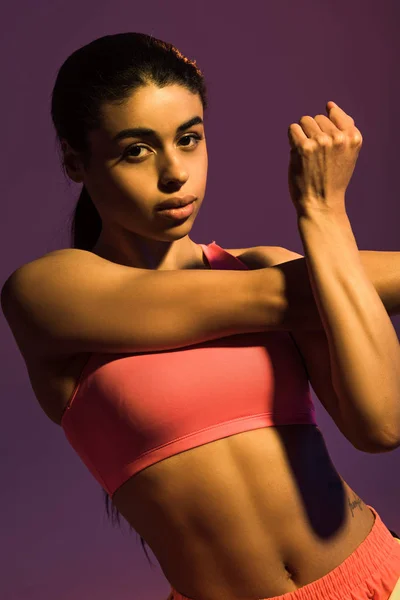 Belle sportive afro-américaine fille échauffement et regarder caméra isolé sur violet — Photo de stock