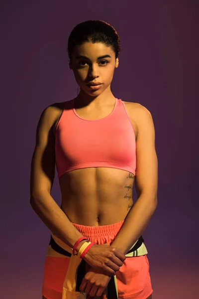 Pretty african american girl in pink sport bra looking at camera on purple background — Stock Photo