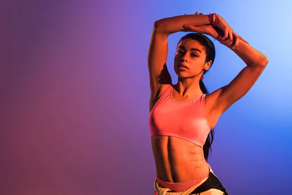 Beautiful african american girl in pink sports bra posing at camera on purple and blue gradient background — Stock Photo