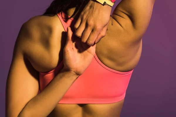 Back view of sportive african american girl in pink sports bra stretching isolated on purple — Stock Photo