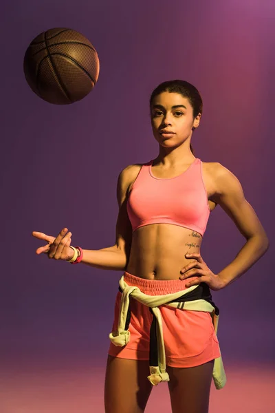 Schöne sportliche afrikanisch-amerikanische Mädchen mit braunem Ball Blick in die Kamera auf lila Hintergrund — Stockfoto