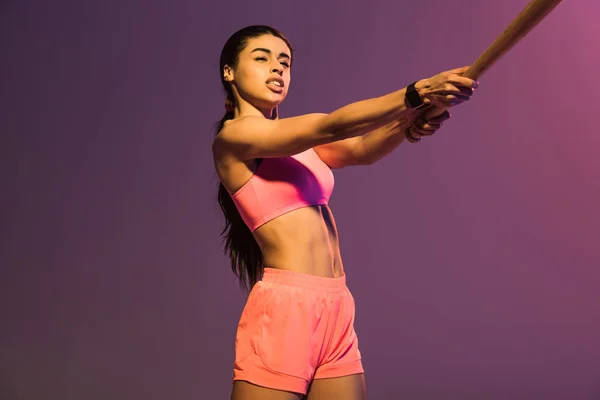 Atraente esportivo menina americana africana em sutiã de esportes rosa jogando beisebol no fundo roxo — Fotografia de Stock