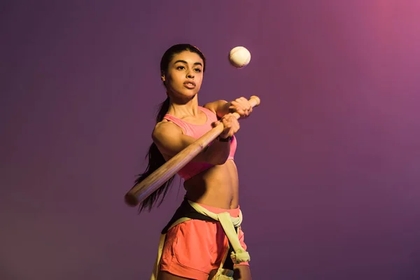 Приваблива спортивна афроамериканська дівчина грає в бейсбол на фіолетовому фоні — стокове фото