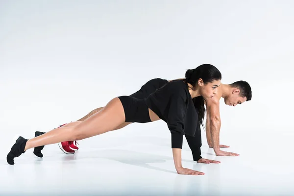 Vista lateral de deportivo multicultural hombre y mujer haciendo flexiones en blanco - foto de stock