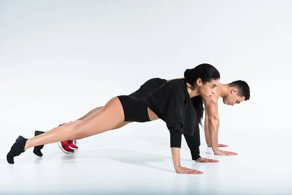 Vista lateral do homem multicultural esportivo e mulher fazendo flexões no branco — Fotografia de Stock