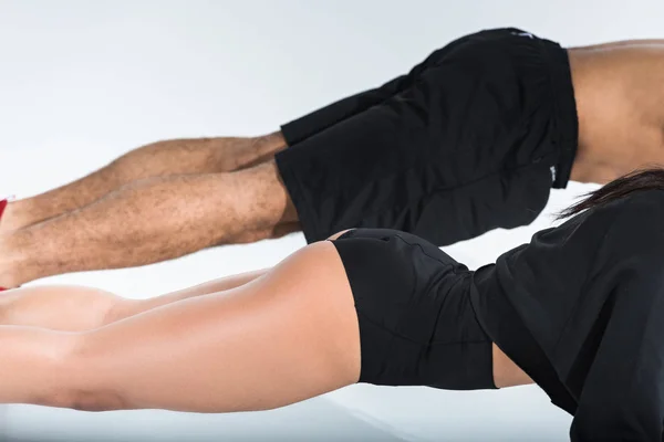 Partial view of man and woman doing push ups on white background — Stock Photo