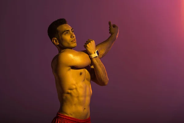 Hombre deportivo guapo en reloj inteligente estiramiento sobre fondo púrpura - foto de stock
