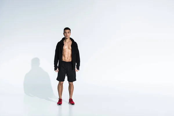 Спортивный смешанной расы человек в черной спортивной куртке, шорты и красные кроссовки на белом фоне — стоковое фото