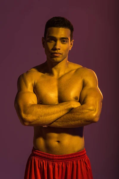 Beau sportif mixte homme posant à la caméra avec les bras croisés sur fond violet — Photo de stock