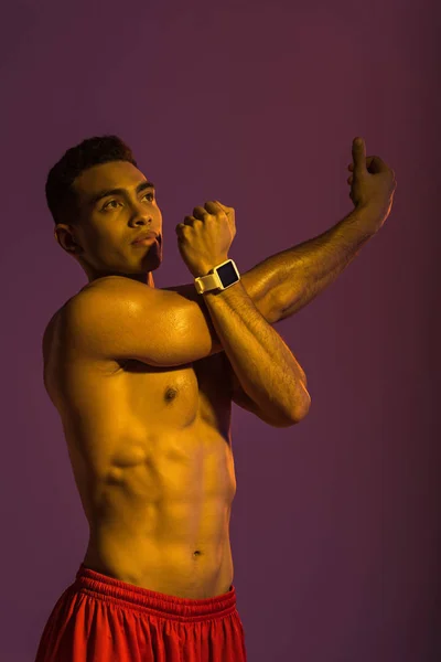 Guapo atlético mestizo raza hombre en inteligente reloj estiramiento sobre púrpura fondo - foto de stock