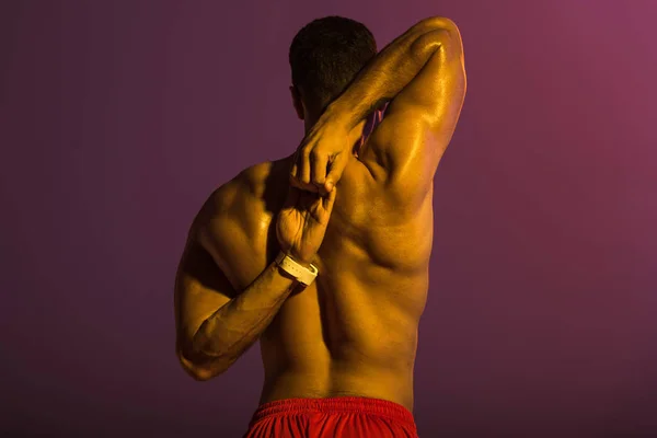 Back view of sportive man with muscular torso stretching on purple background — Stock Photo