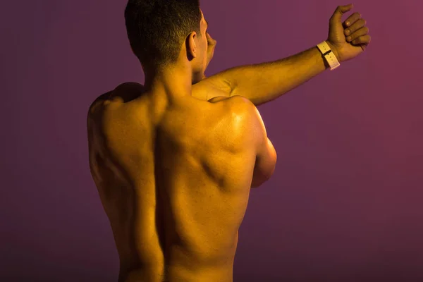Back view of athletic man with muscular torso stretching on purple background — Stock Photo