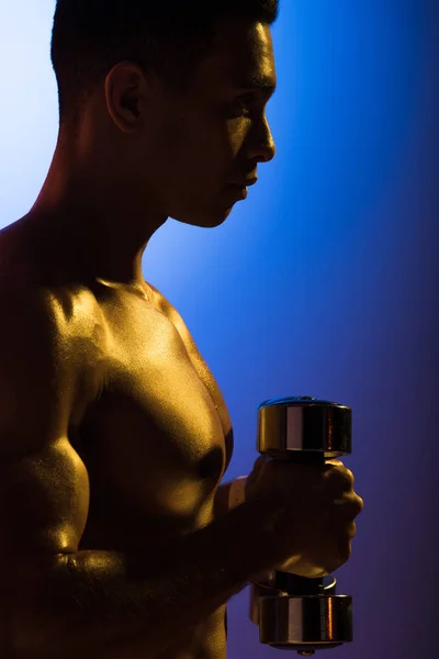 Side view of sportive mixed race man with dumbbell on blue and dark purple gradient background — Stock Photo