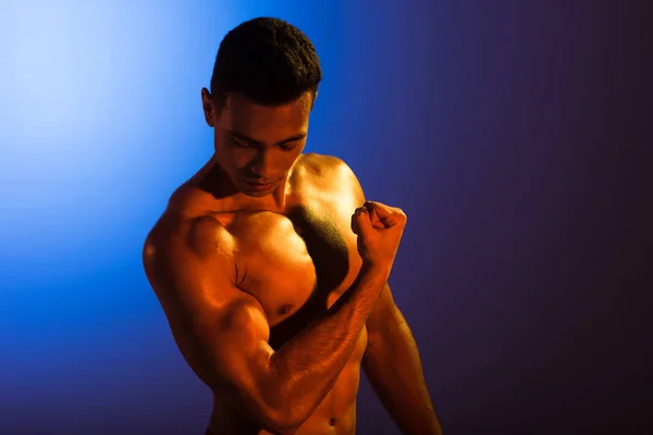 Handsome athletic mixed race man demonstrating biceps on blue and dark purple gradient background — Stock Photo