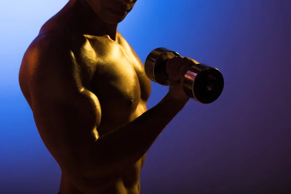 Vista recortada del hombre atlético con mancuerna sobre fondo degradado azul y púrpura oscuro - foto de stock