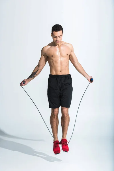 Handsome sportive mixed race man jumping with skipping rope on white — Stock Photo