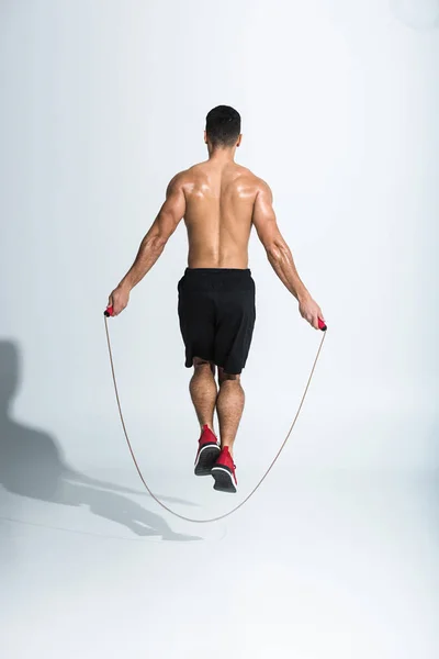 Back view of athletic man in black shorts jumping with skipping rope on white — Stock Photo