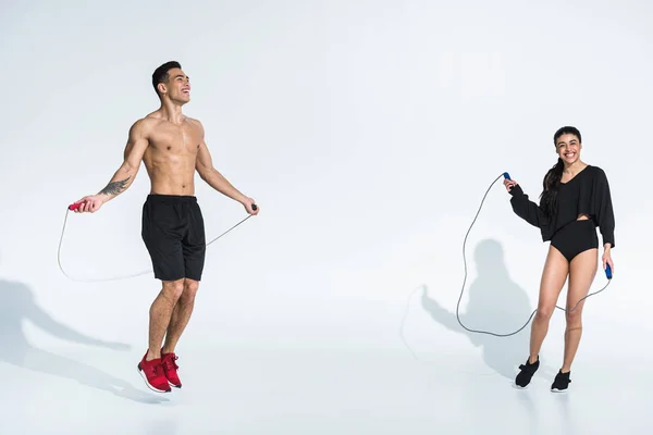 Smiling african american girl and handsome mixed race man training with jump ropes on white background — Stock Photo