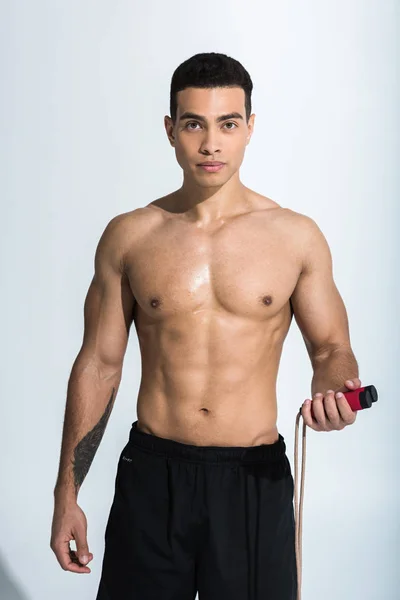 Handsome mixed race man with muscular torso holding jump rope and looking at camera on white — Stock Photo