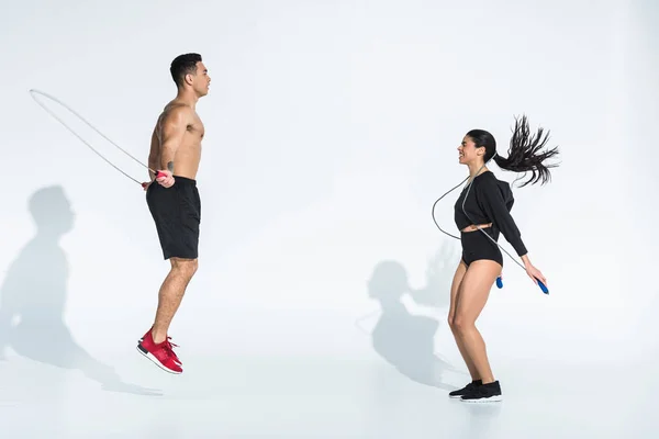 Smiling african american woman and athletic mixed race man training with jump ropes on white — Stock Photo