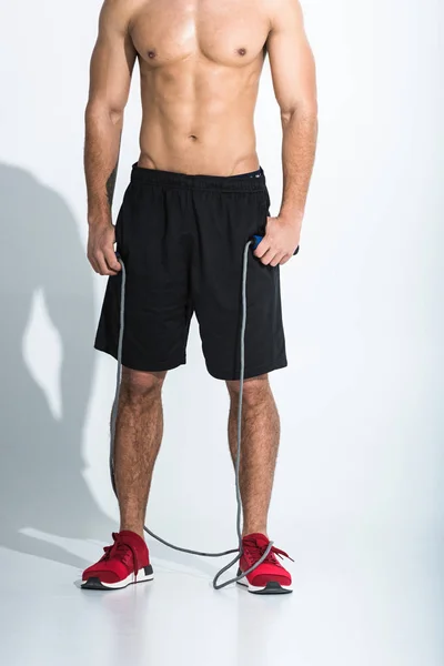 Vista parcial del hombre en pantalones cortos negros y zapatillas rojas sosteniendo la cuerda de salto en blanco - foto de stock