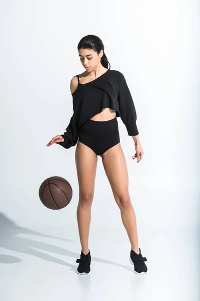 Довольно африканская американка в черной спортивной одежде и кроссовках, играющая в мяч на белом — стоковое фото