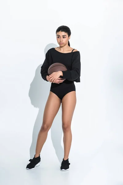 Chica americana bastante africana en ropa deportiva negra y zapatillas de deporte sosteniendo la bola en blanco - foto de stock