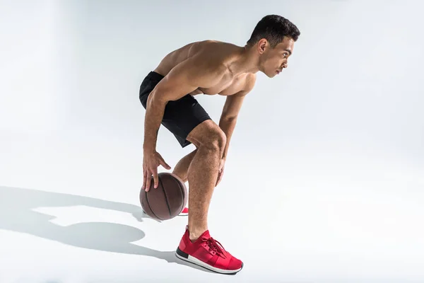 Bello uomo razza mista in scarpe da ginnastica rosse giocare a palla su sfondo bianco — Foto stock