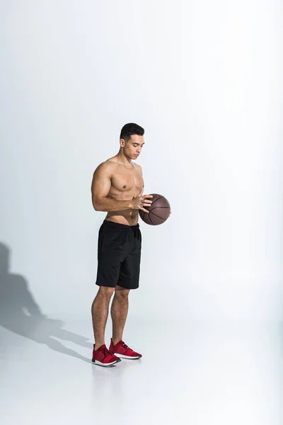 Handsome shirtless mixed race man in black shorts and red sneakers holding ball on white — Stock Photo