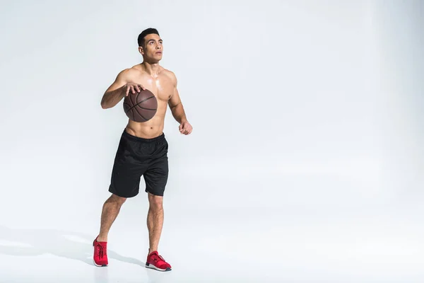Bello atletico uomo gara mista in pantaloncini neri e scarpe da ginnastica rosse giocare a palla su bianco — Foto stock