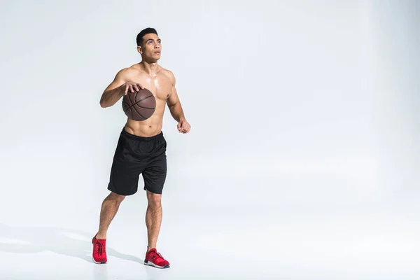 Guapo atlético mestizo hombre de raza en pantalones cortos negros y zapatillas rojas jugando pelota en blanco - foto de stock