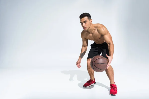 Handsome sportive mixed race man in red sneakers playing ball on white — Stock Photo