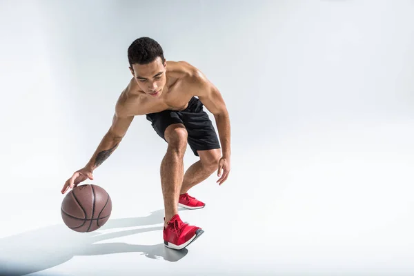 Good-looking sportive mixed race man in red sneakers playing ball on white — Stock Photo