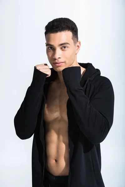 Handsome mixed race man in black sports jacket warming up and looking at camera on white — Stock Photo