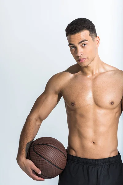 Hombre de raza mixta atlético bien parecido con torso muscular celebración de bola marrón y mirando a la cámara en blanco - foto de stock