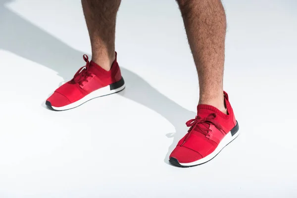 Recortado vista de hombre deportivo en zapatillas de deporte rojas sobre fondo blanco - foto de stock
