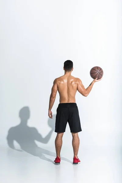 Visão traseira do homem atlético em shorts pretos segurando bola marrom no fundo branco — Fotografia de Stock