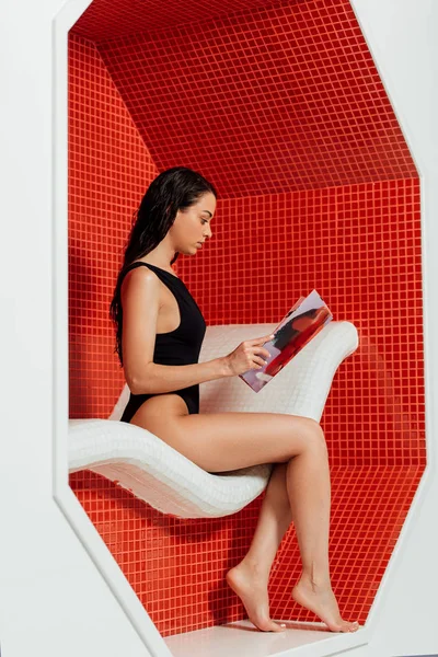 Side view of pretty woman in black swimsuit reading magazine in spa center — Stock Photo