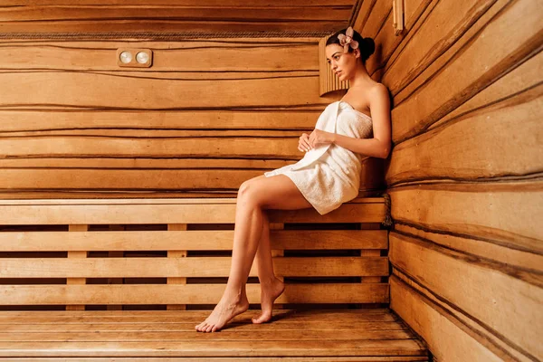 Sonriente chica descalza en toalla con flor en pelo en sauna - foto de stock