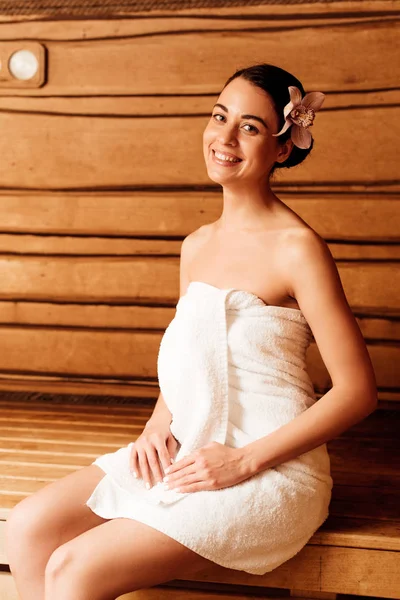 Smiling girl with flower in hair looking at camera in sauna — Stock Photo