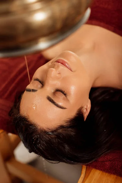 Overhead view of woman lying under shirodhara vessel during ayurvedic procedure — Stock Photo