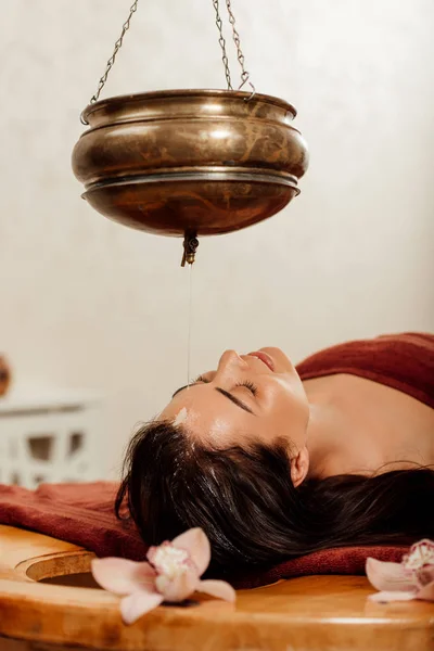 Rilassata giovane donna sdraiata sotto vaso shirodhara durante la procedura ayurvedica — Foto stock