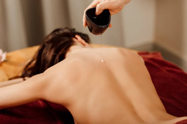 Vista parziale del massaggiatore versando olio essenziale sul retro nel centro benessere — Foto stock
