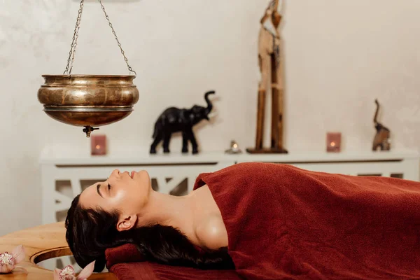 Side view of woman lying under shirodhara vessel during ayurvedic procedure — Stock Photo