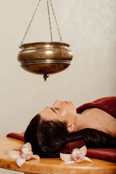 Relaxed young woman lying under shirodhara vessel during ayurvedic procedure — Stock Photo