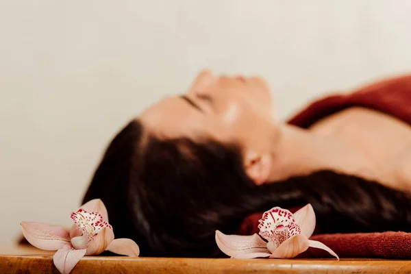 Enfoque selectivo de la mujer acostada en la mesa de masaje con flores - foto de stock